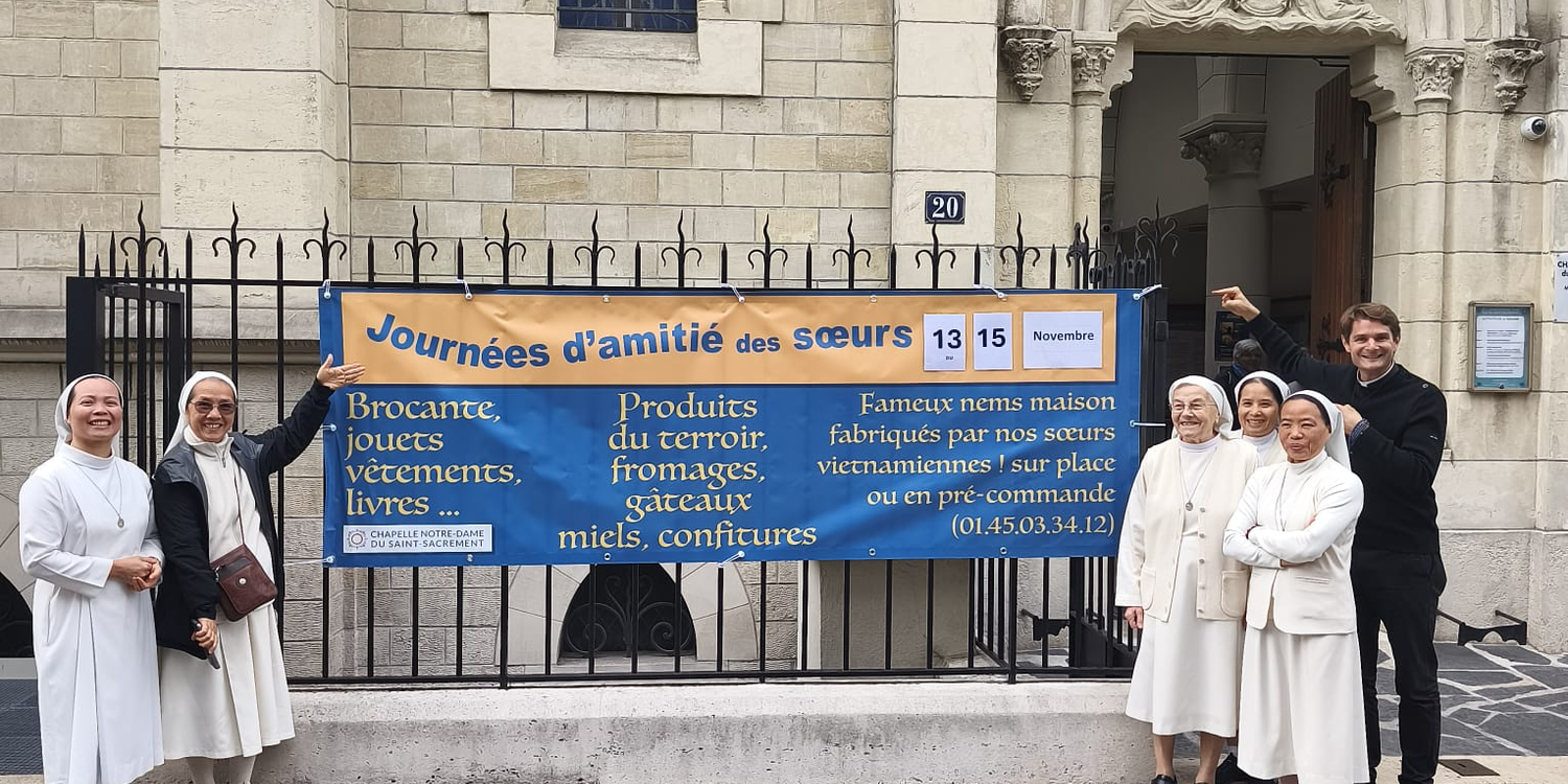 Journées d’Amitié des Sœurs novembre 2026 Les sœurs et le prêtre devant la chapelle, autour de la banderole des Journées d'amitié du 13 au 15 novembre
